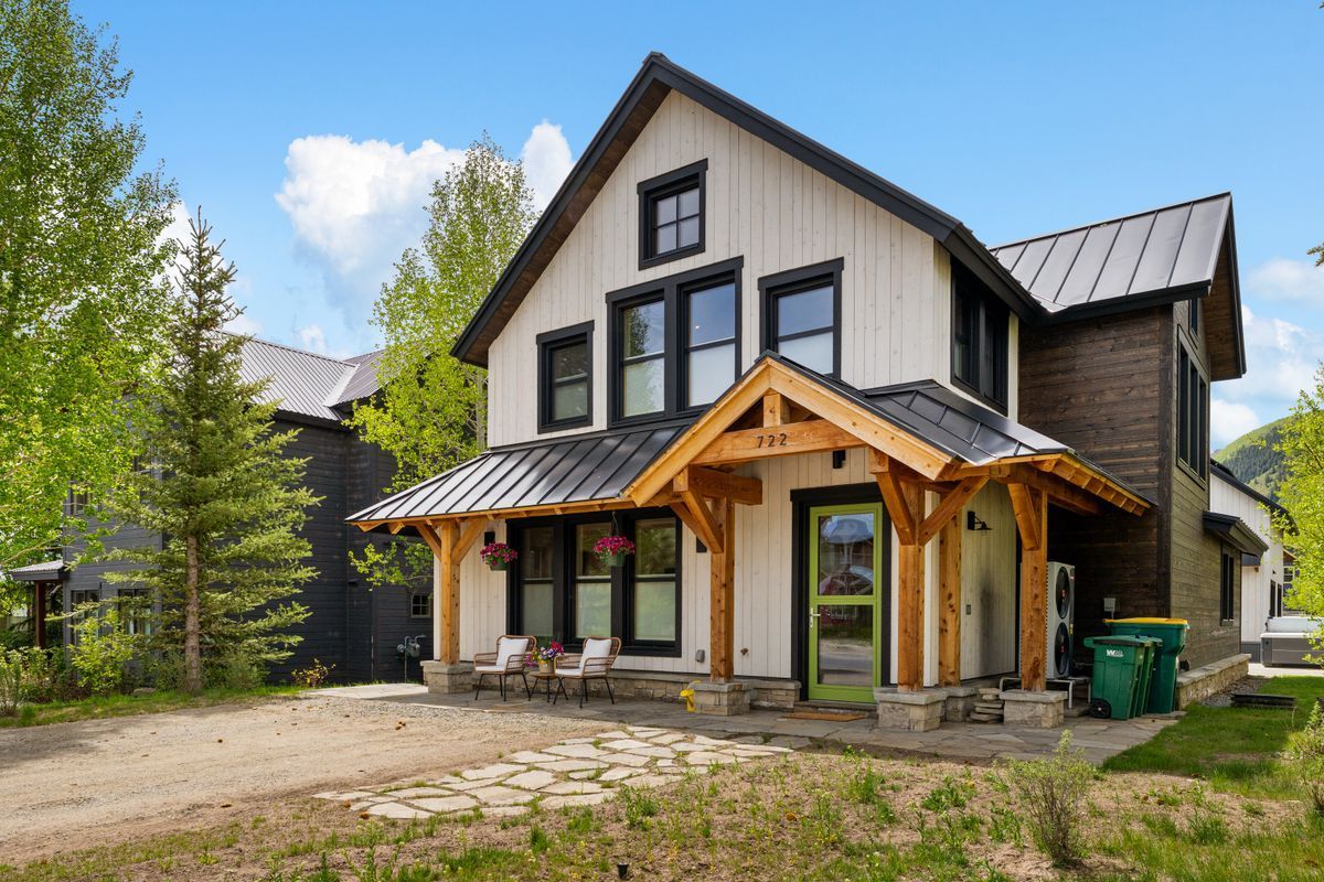Modern two-story farmhouse with white siding, dark roof, and wooden porch in a sunny yard