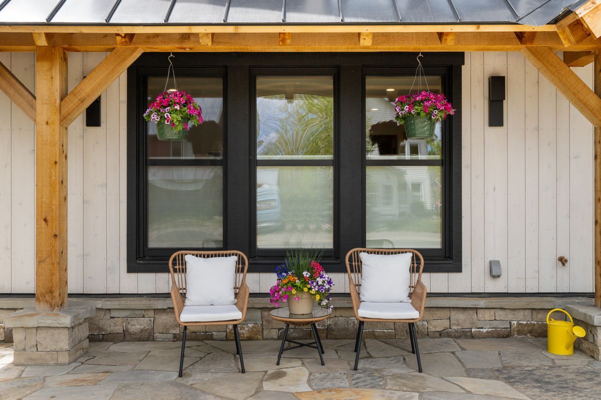 Front porch with two white chairs, hanging flower baskets, and a dark-framed window on a white house