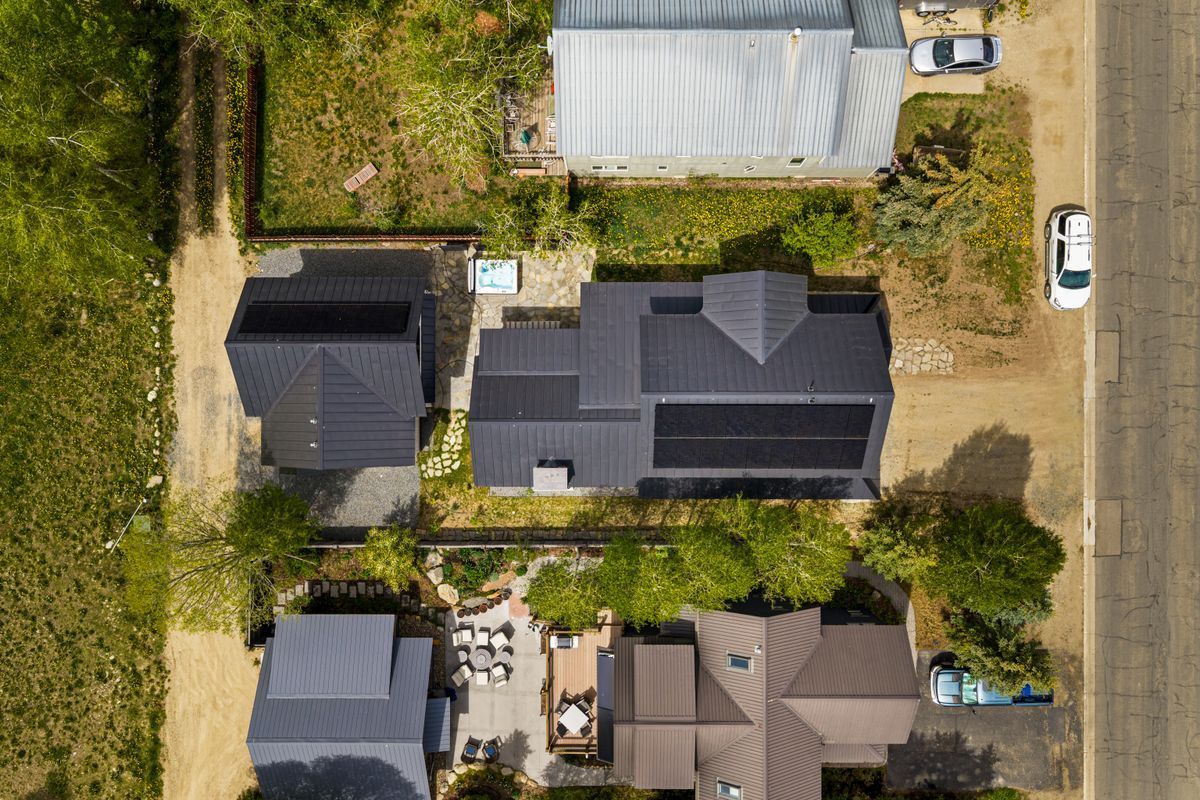 Aerial view of a suburban neighborhood with rooftops, driveways, trees, and a road along the right side.