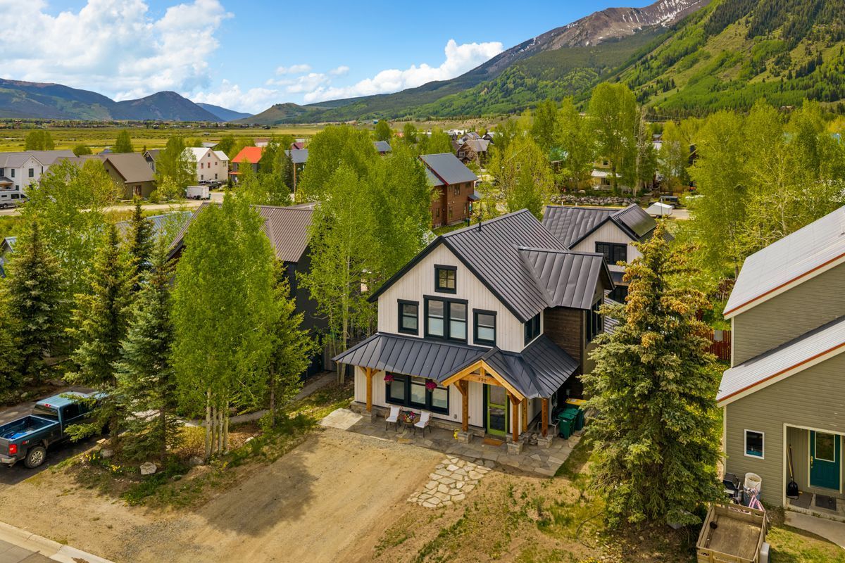 Mountain cabin neighborhood with a white house, pine trees, and mountains in the background