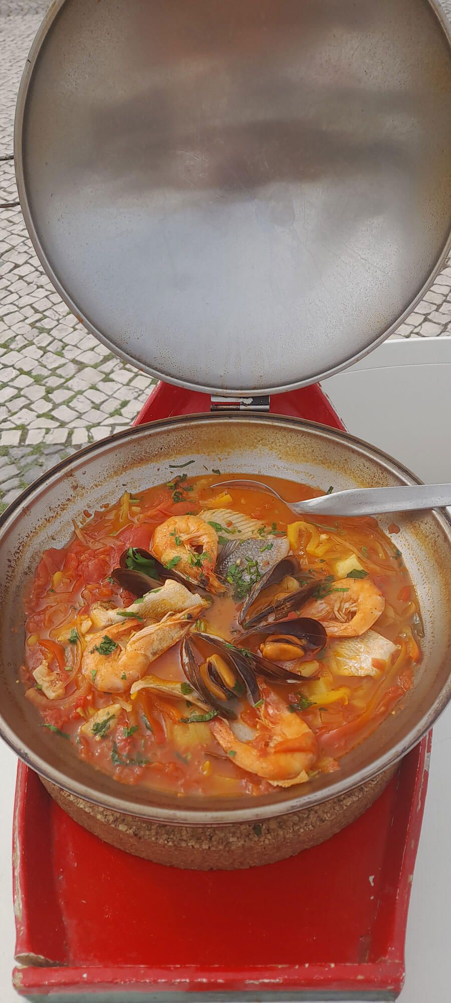 Auf einem roten Tablett steht ein Topf Suppe mit Garnelen, Muscheln und Tomaten, portugiesischer Fischeintopf