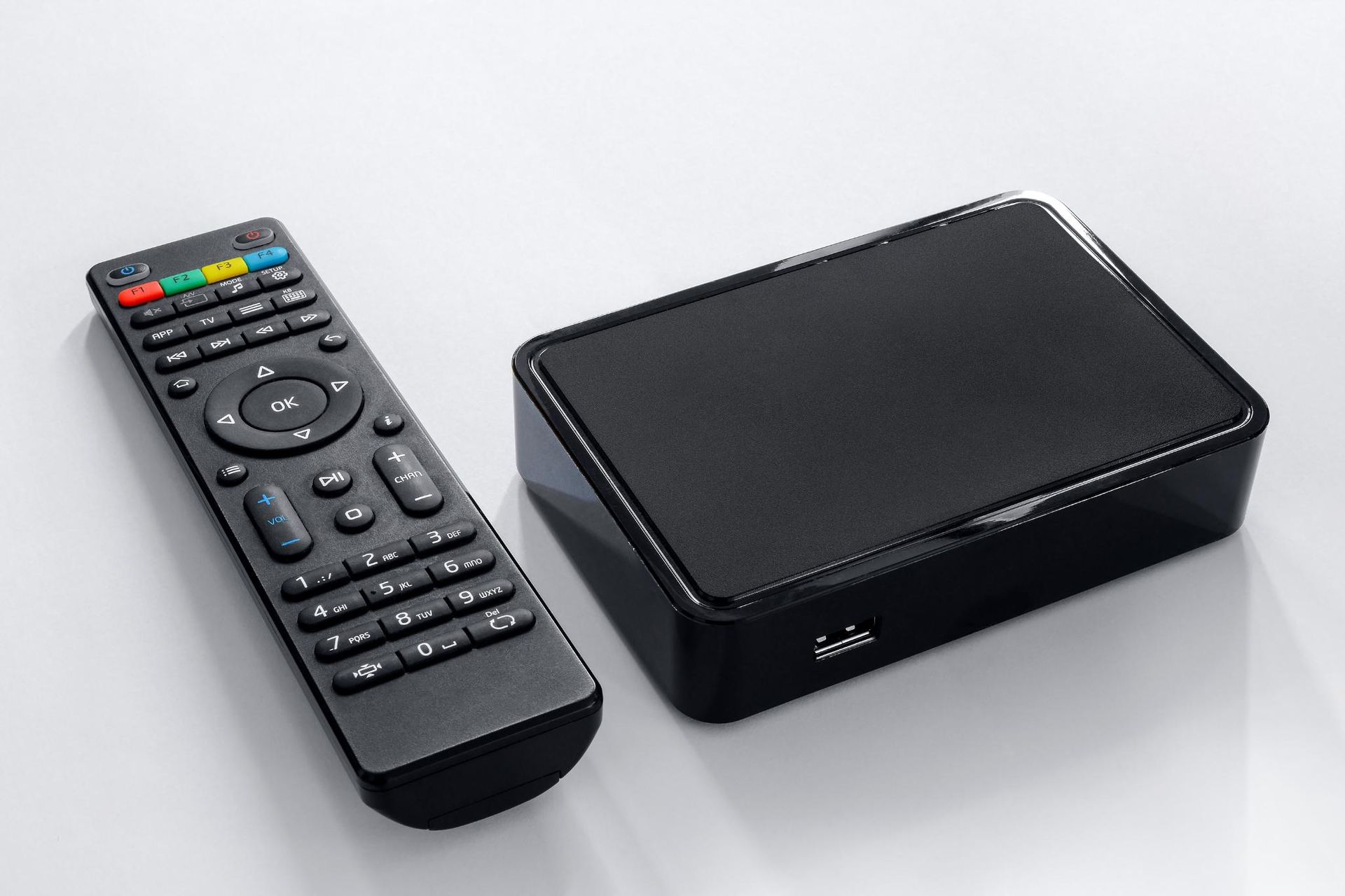 Black media streaming box beside a black remote control on a white surface