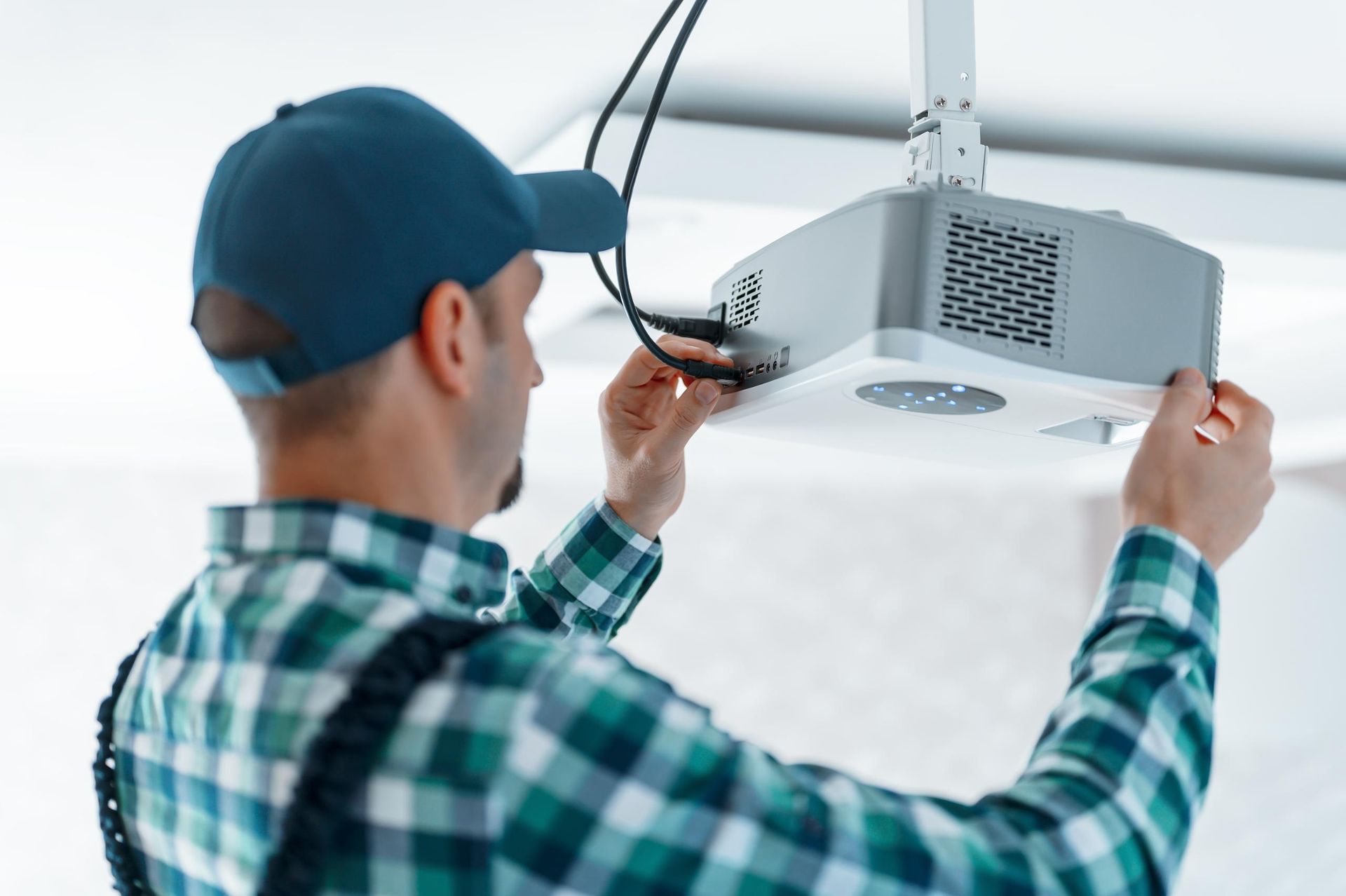Technician installing a ceiling-mounted projector, adjusting cables in a room