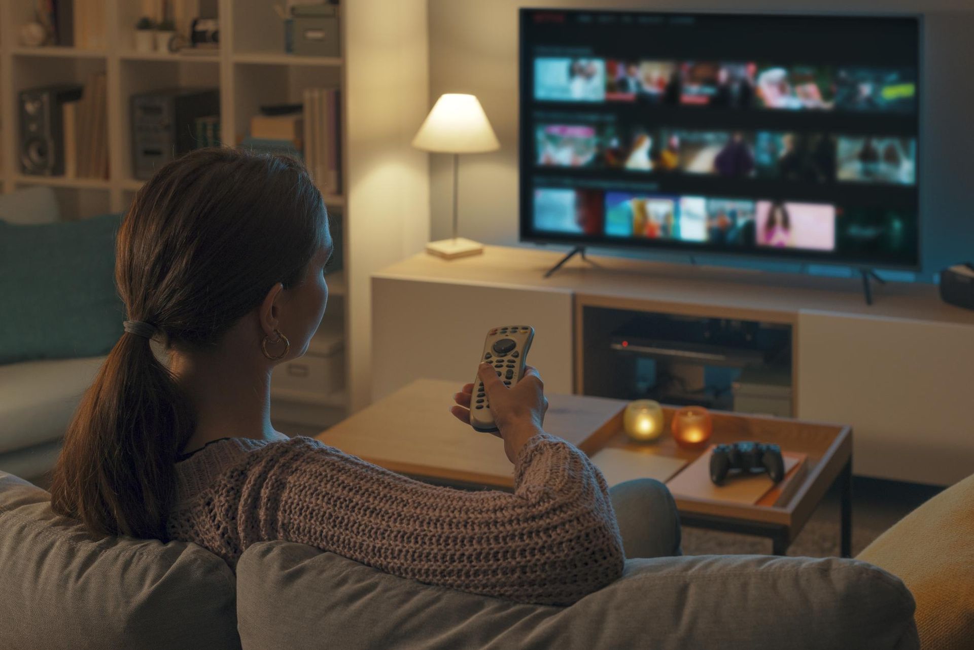 Person on couch watching a streaming TV with a remote in a cozy living room at night