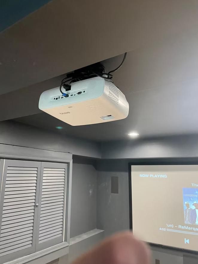 Ceiling-mounted projector in a gray home theater room, projecting onto a screen.