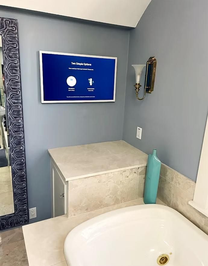 Bathroom with wall-mounted screen above a tiled shelf, sink basin, and gray walls.