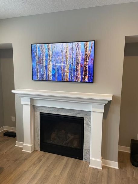 Modern living room fireplace with white mantel and wall-mounted TV showing a blue forest scene.