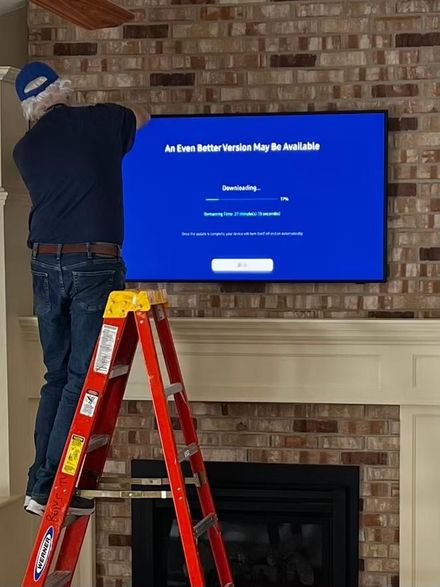 Person installing a wall-mounted TV above a fireplace in a brick living room.