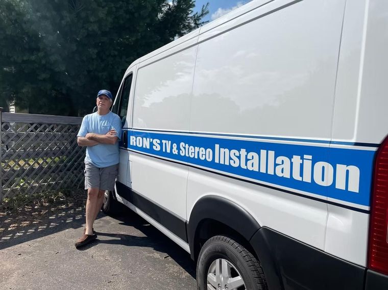 Man leaning against white installation van with blue stripe and text on the side