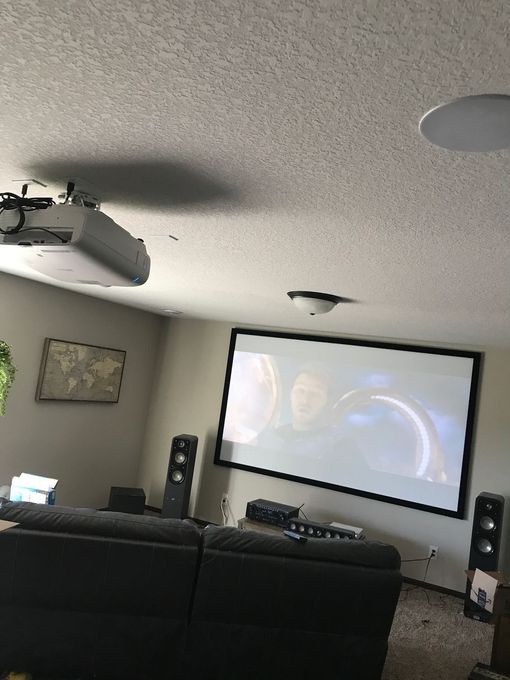 Luxury home theater with beige reclining seats, wood paneling, and a large projection screen