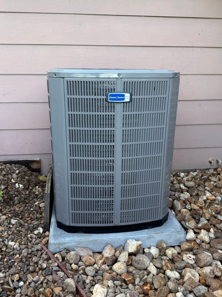 Two white outdoor air conditioning units beside a building on a gravel bed