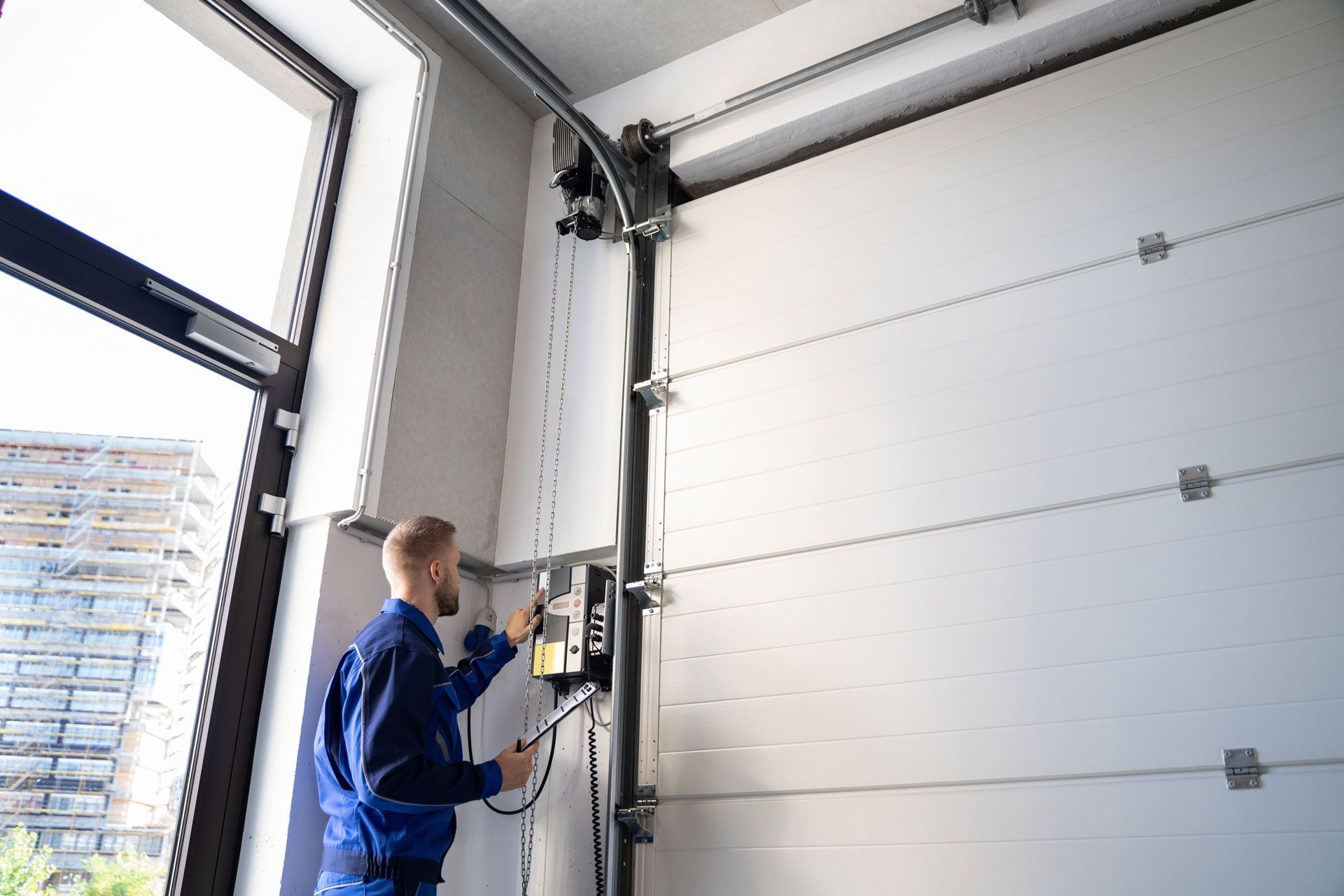 Technician operating a garage door opener beside a large white sectional door