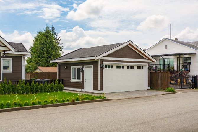 Single-story suburban house with a double garage, brown trim, and a small front lawn on a quiet street.