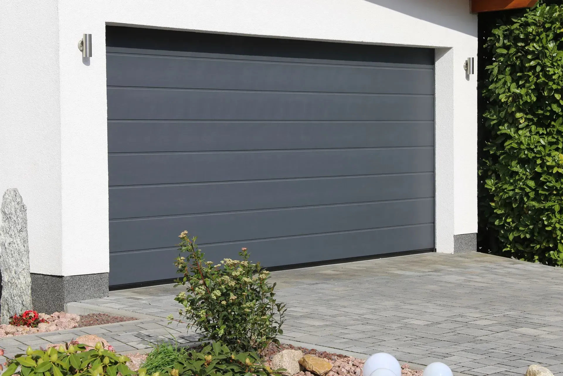 A gray garage door is sitting in front of a white house.