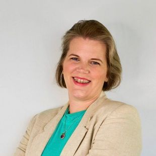 A woman wearing a white jacket and a necklace is smiling for the camera.