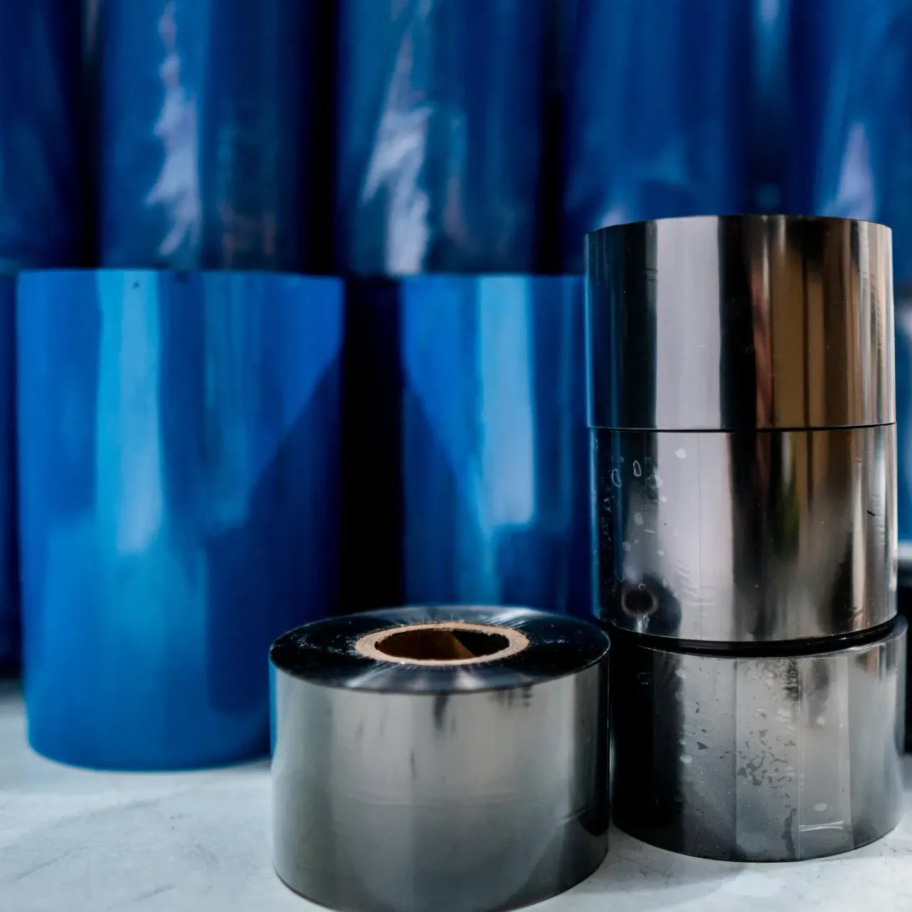Glänzende, metallische Filmrollen und blaue, durchscheinende Rollen stapeln sich vor einem blauen Hintergrund