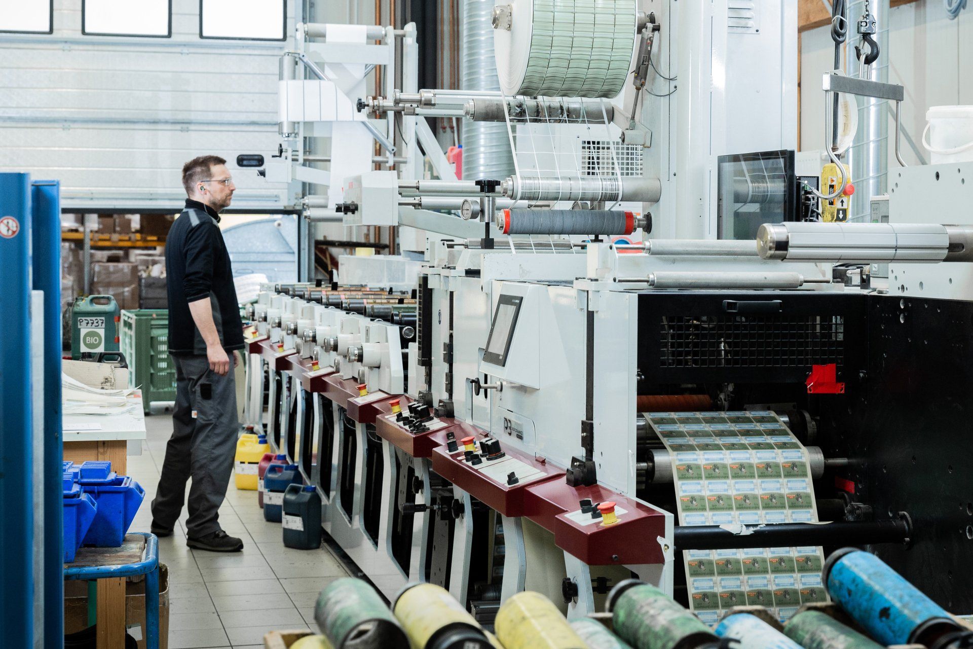 Mann im schwarzen Hemd neben einer großen industriellen Druckmaschine in einer Fabrik
