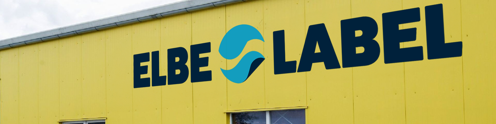 Gelbe Gebäudefassade mit blauem ELBE SLABEL-Schild und Logo