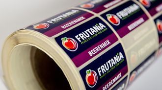 Nahaufnahme eines gerollten Etiketts mit lila FRUTANIA-Schriftzug und Apfellogos auf weißem Hintergrund