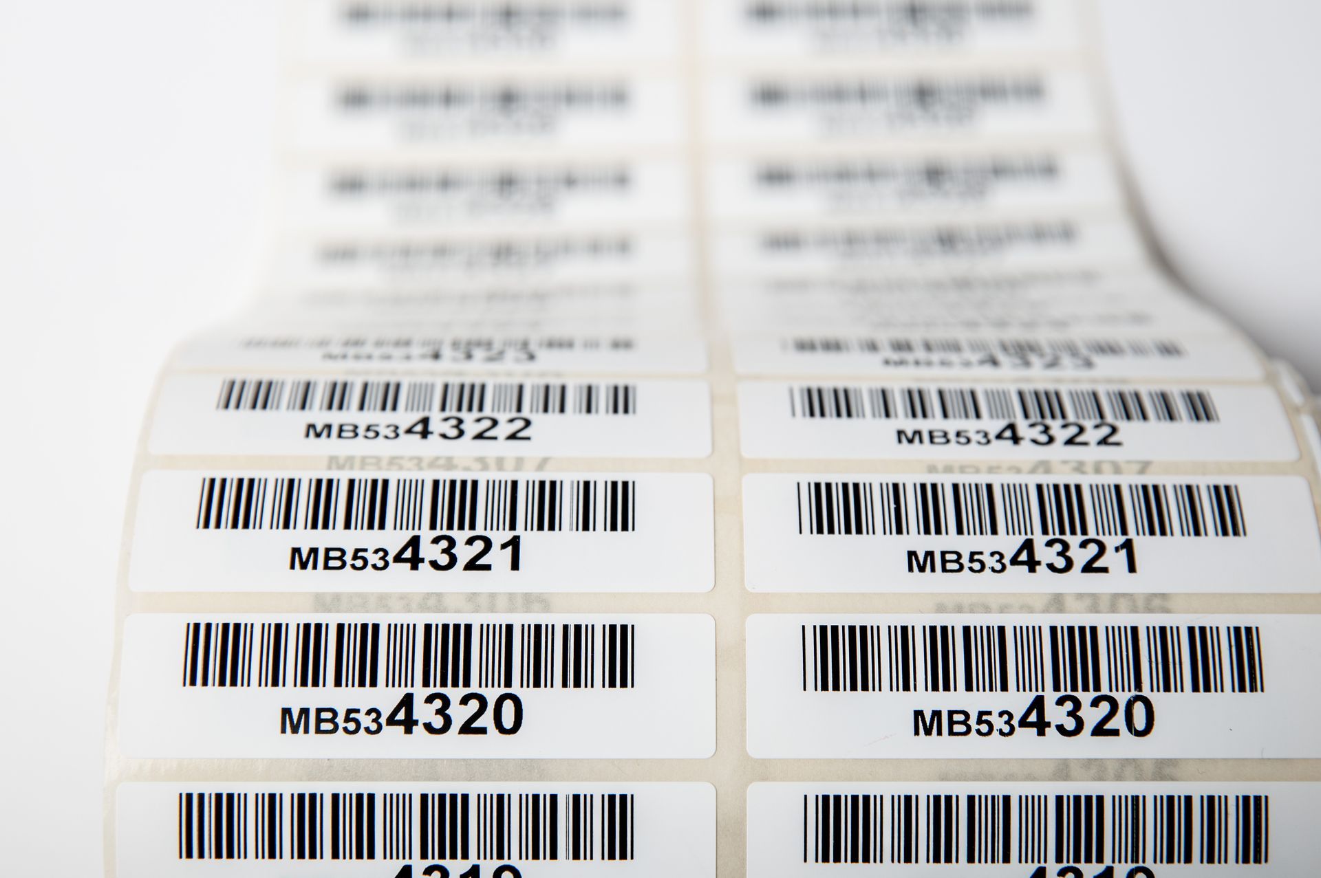 Gestapelte Barcode-Etiketten mit Nummern auf weißen Blättern in einem Drucker oder Etikettenspender.