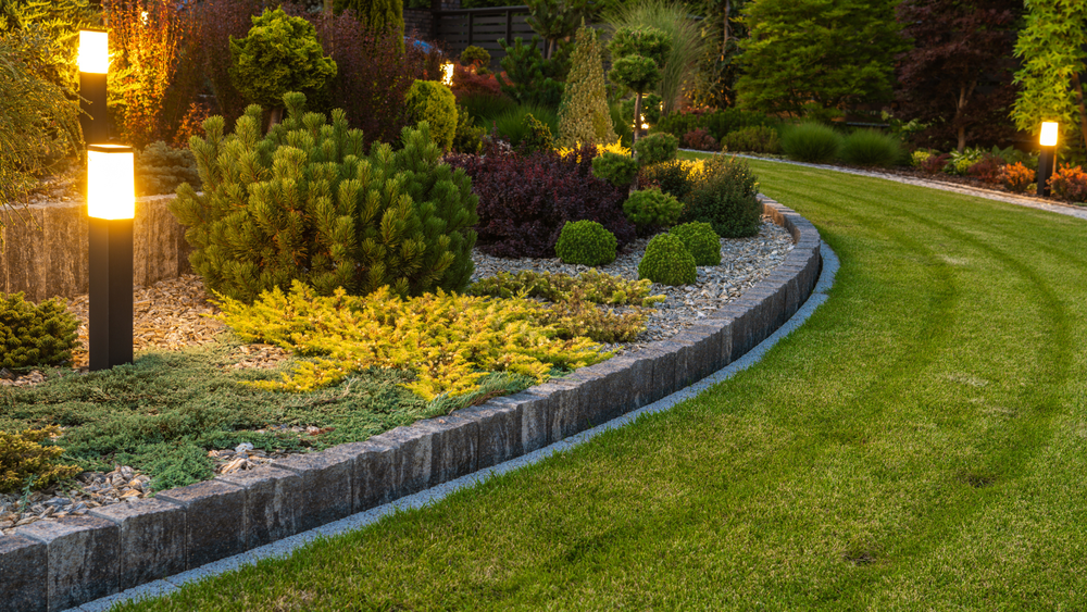 Lush garden with trimmed green grass, colorful plants, and illuminated pathway lights.