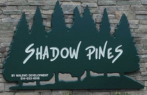 Shadow Pines sign on a stone wall, with green pine silhouettes and white lettering