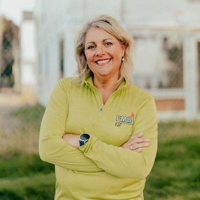 Smiling person in a light green jacket standing outdoors with arms crossed.
