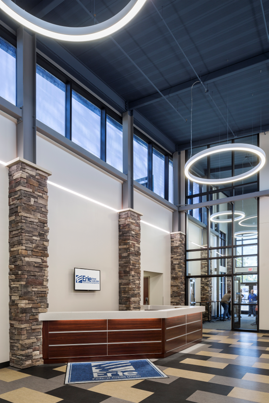 Modern lobby with high windows, circular ceiling lights, reception desk, and glass entry doors