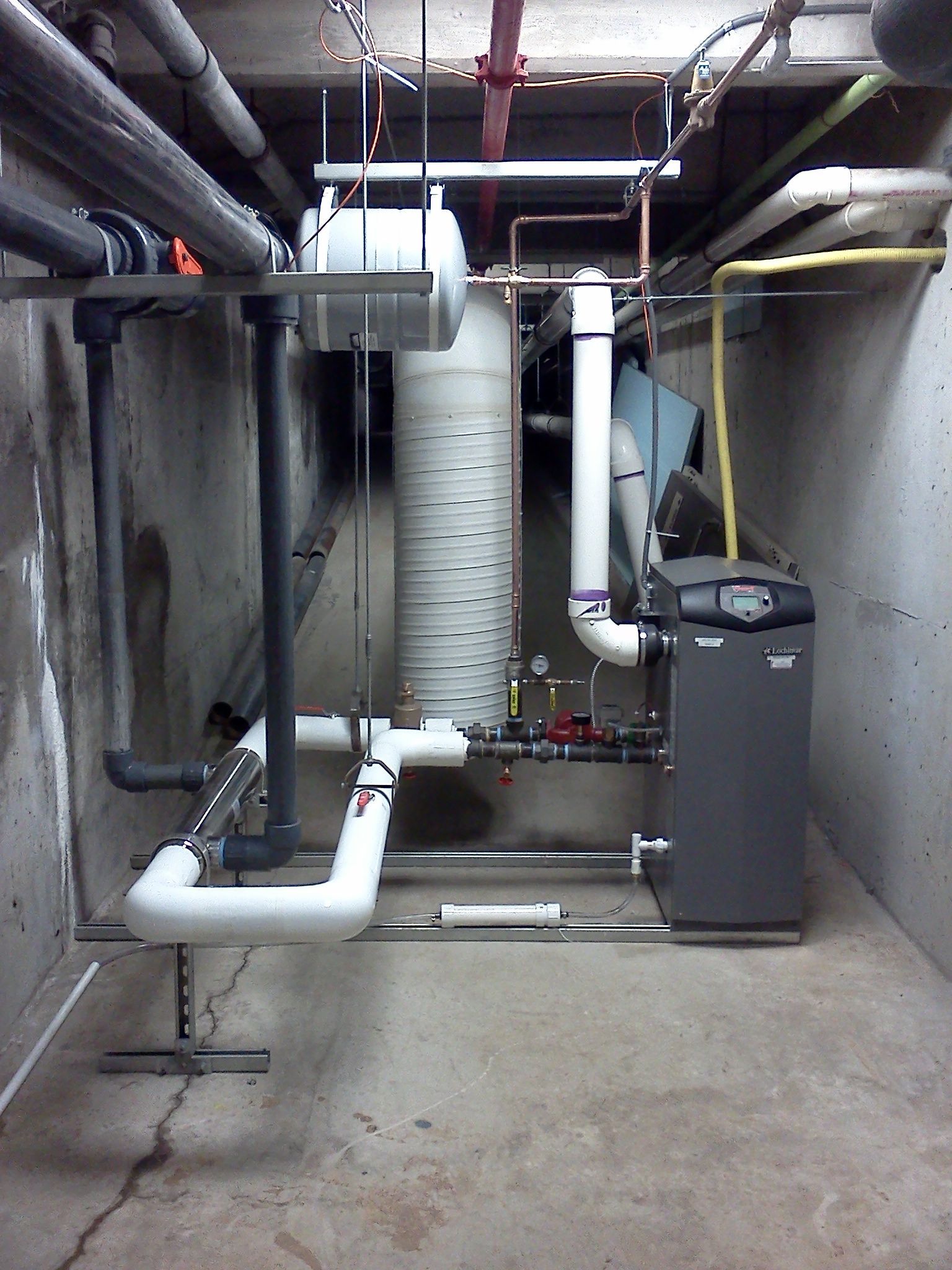 Industrial basement utility room with pipes, ducts, and a large water heater or boiler system.