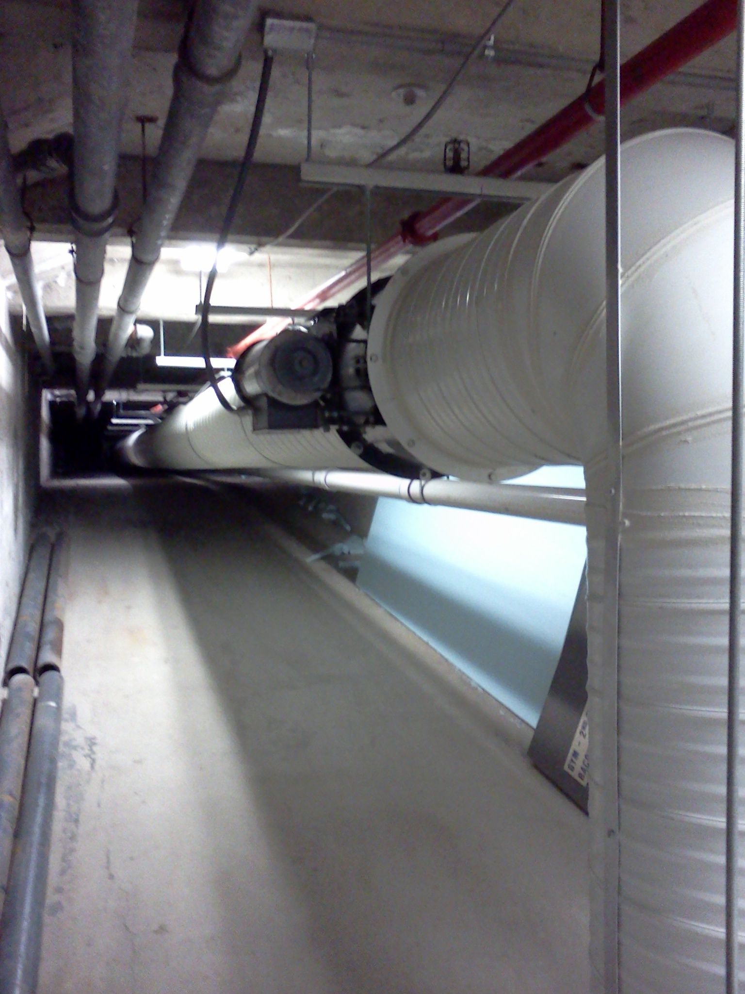 Industrial utility tunnel with large white pipes and overhead ductwork