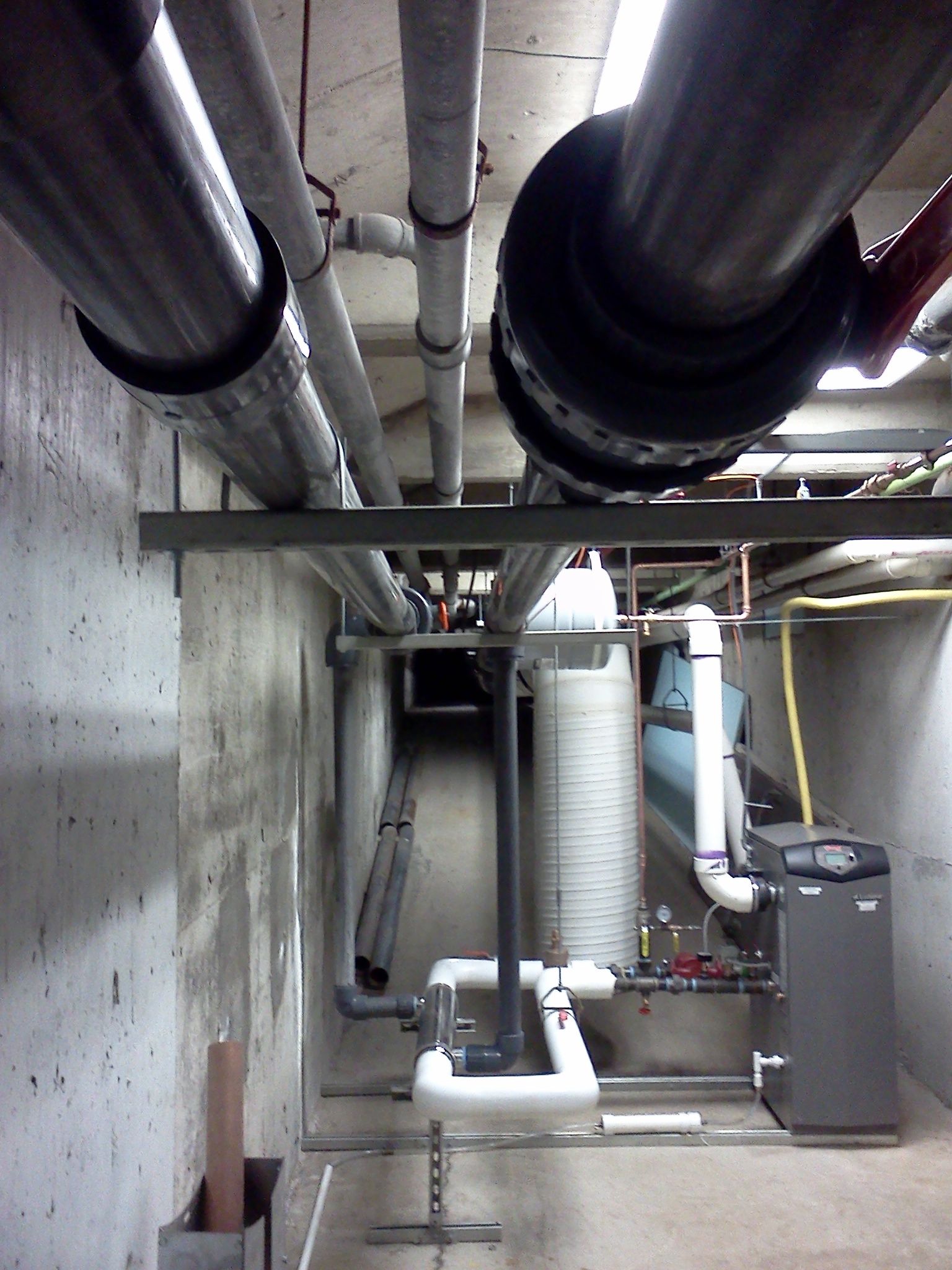 Basement utility room with exposed pipes, ducts, and heating equipment along concrete walls