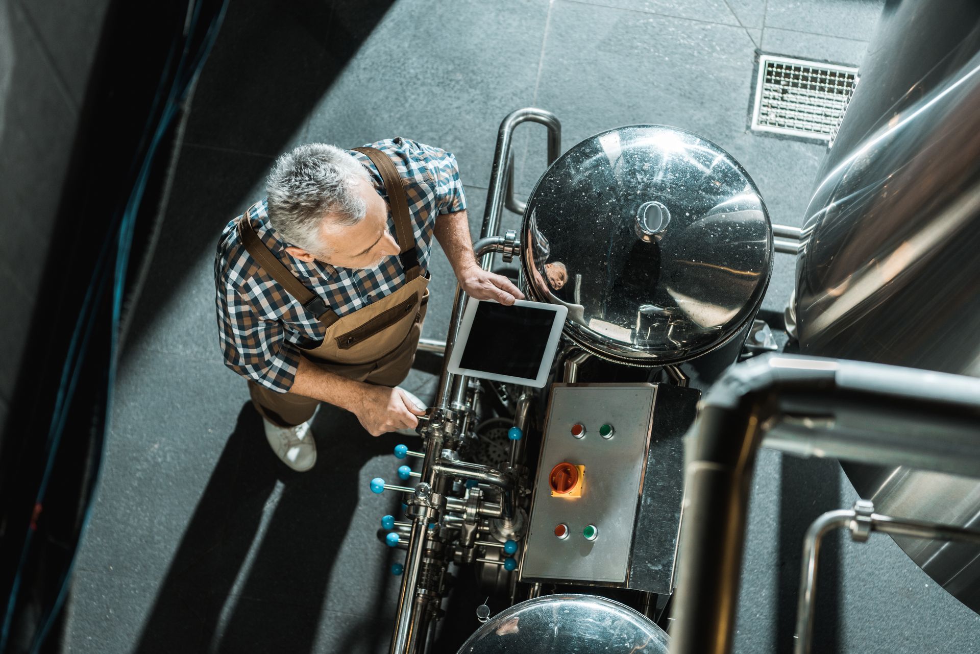 Person inspecting equipment beside large metal tanks in a narrow industrial space