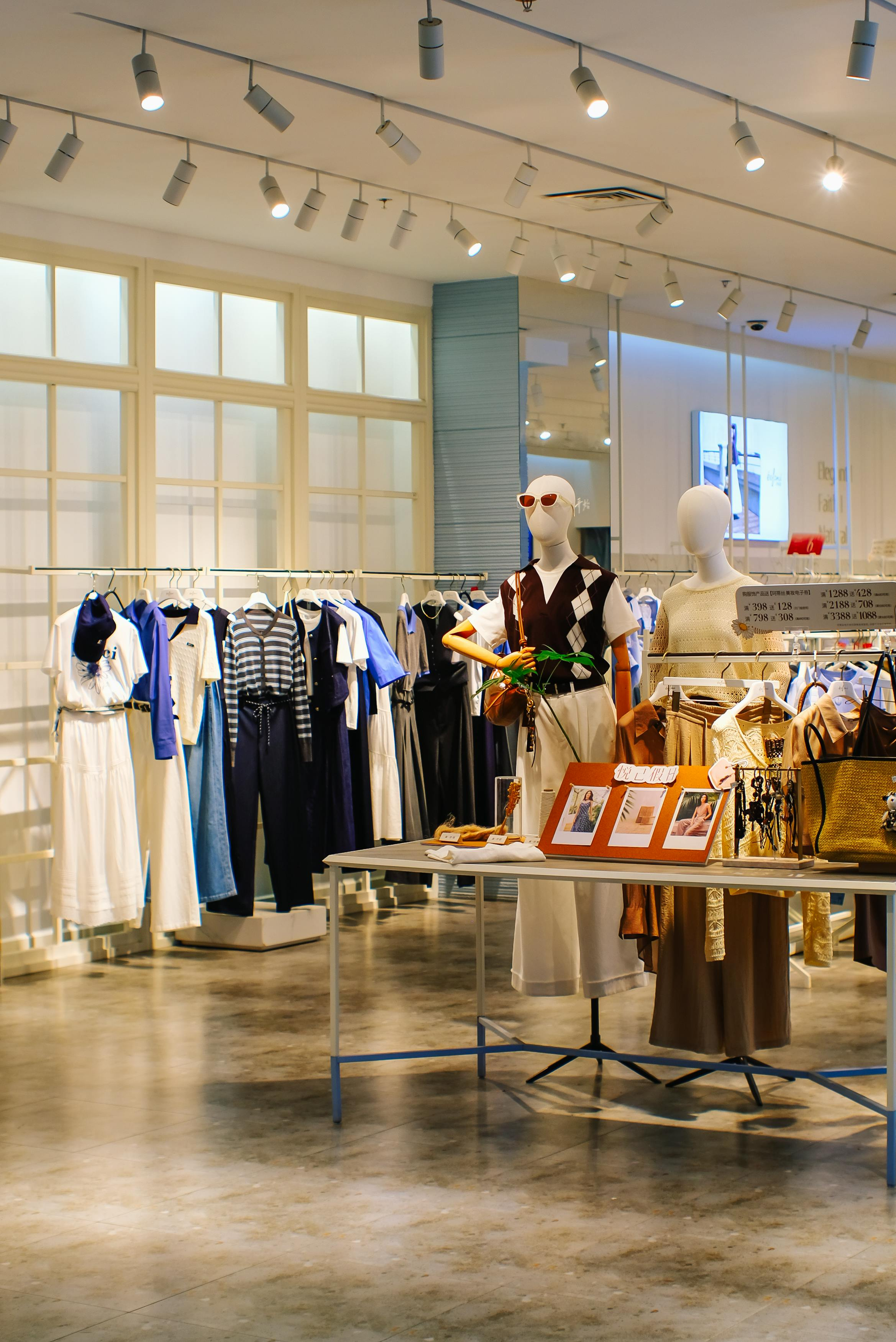 Clothing store interior with racks of white and blue dresses and a mannequin display under track lighting
