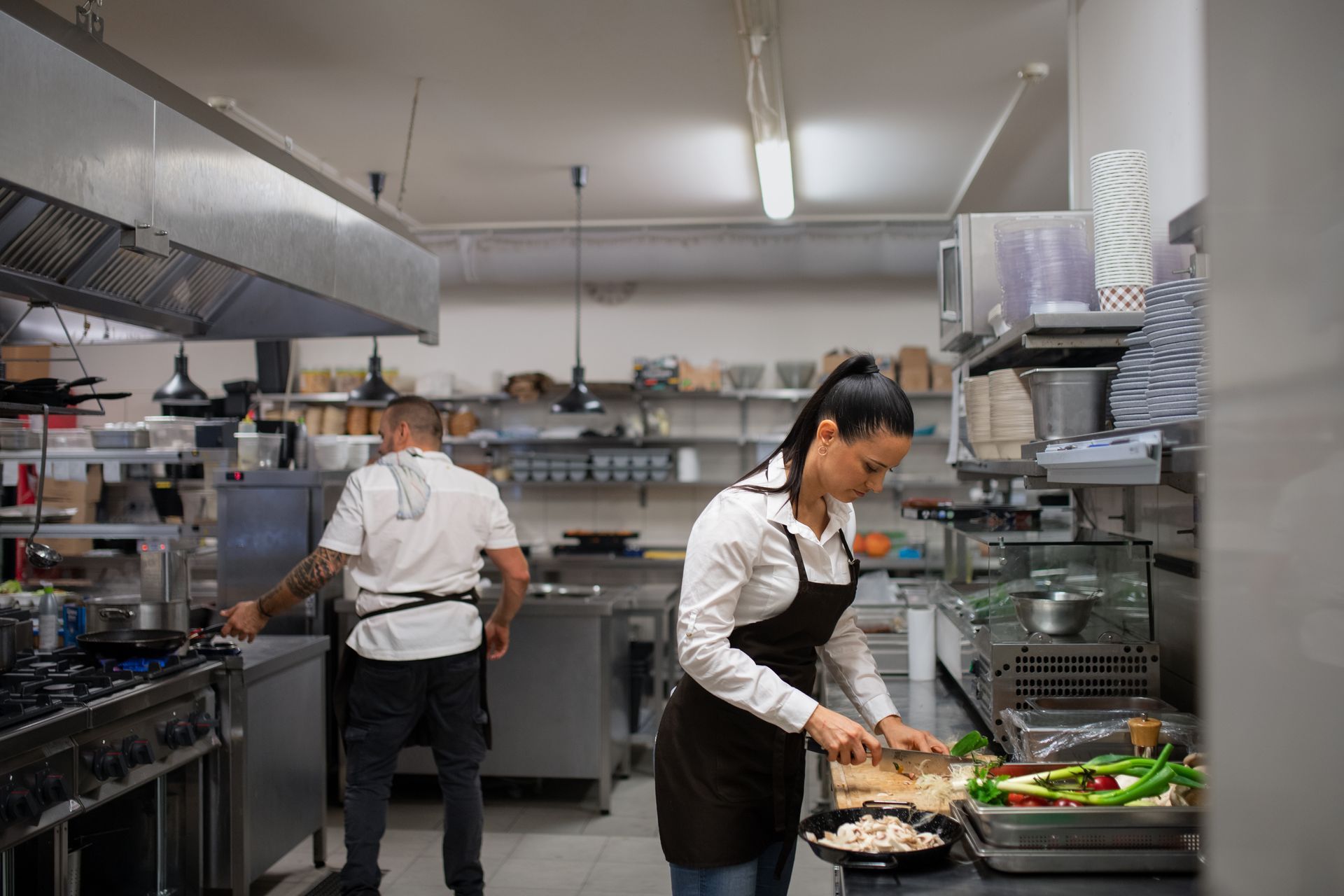 Commercial kitchen with two chefs preparing food at stainless-steel counters.