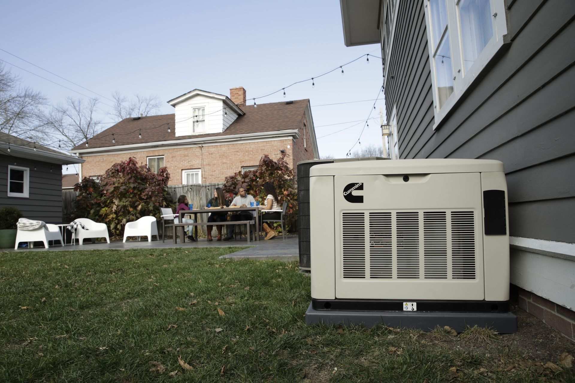 Backyard lawn with beige generator beside house, patio furniture, and brick home in background