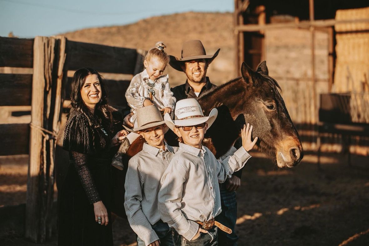 Family posing with a horse and donkey in a rustic ranch setting, with one child waving.