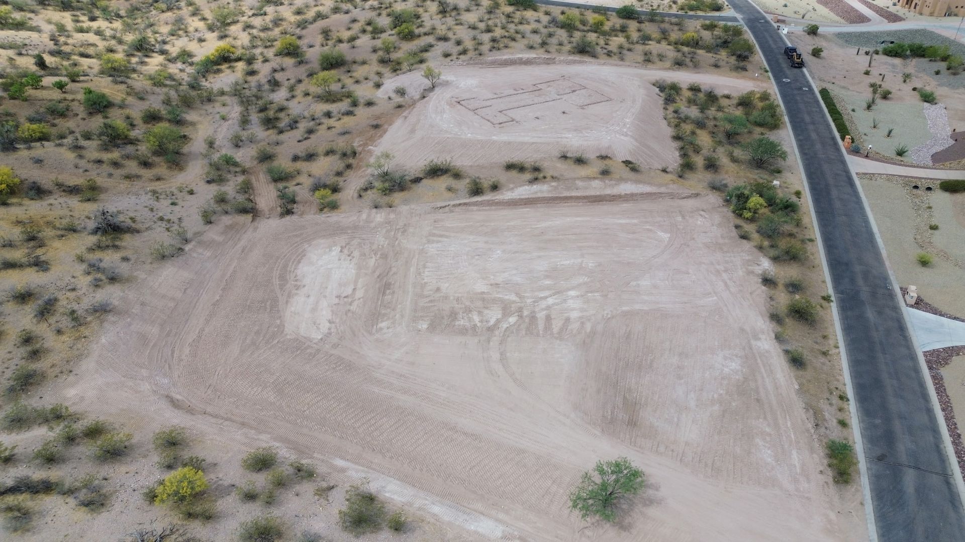Aerial view of a desert lot with graded dirt and a paved road along the right side.