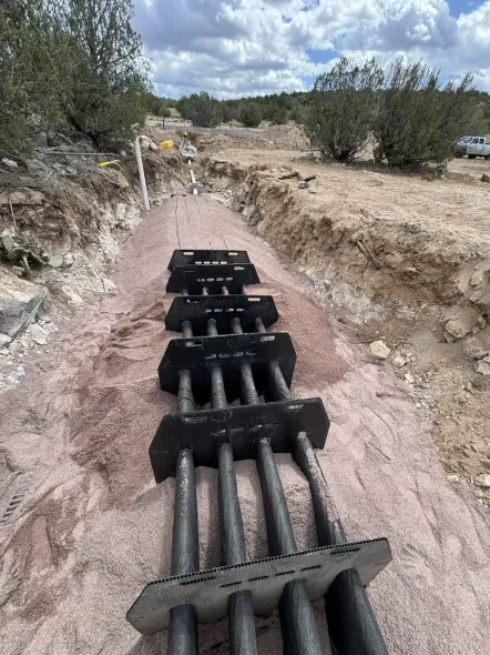 Construction trench with large black cable conduit running through a dug-out rocky path outdoors