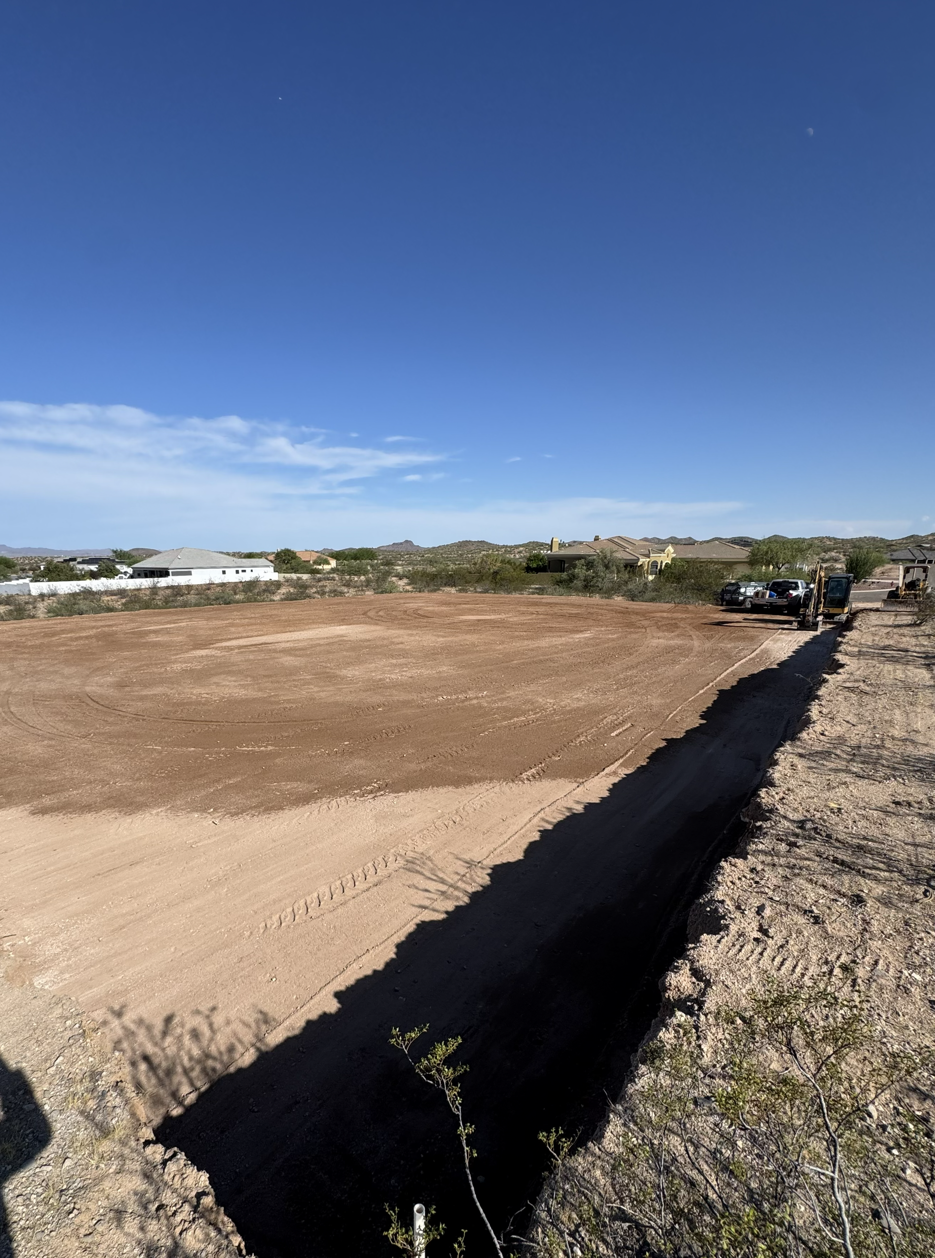 Open dirt lot under a blue sky with a low wall and distant buildings on the horizon.