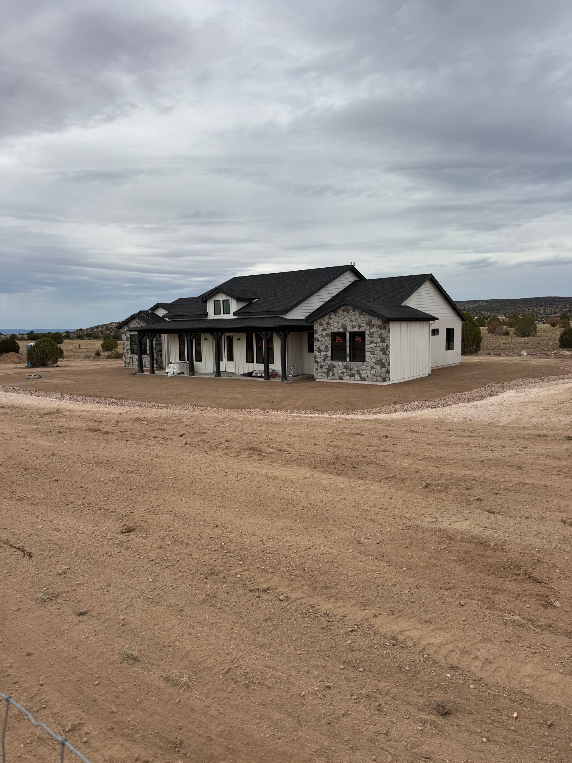 Stone house with dark roof on a dusty lot under a cloudy sky