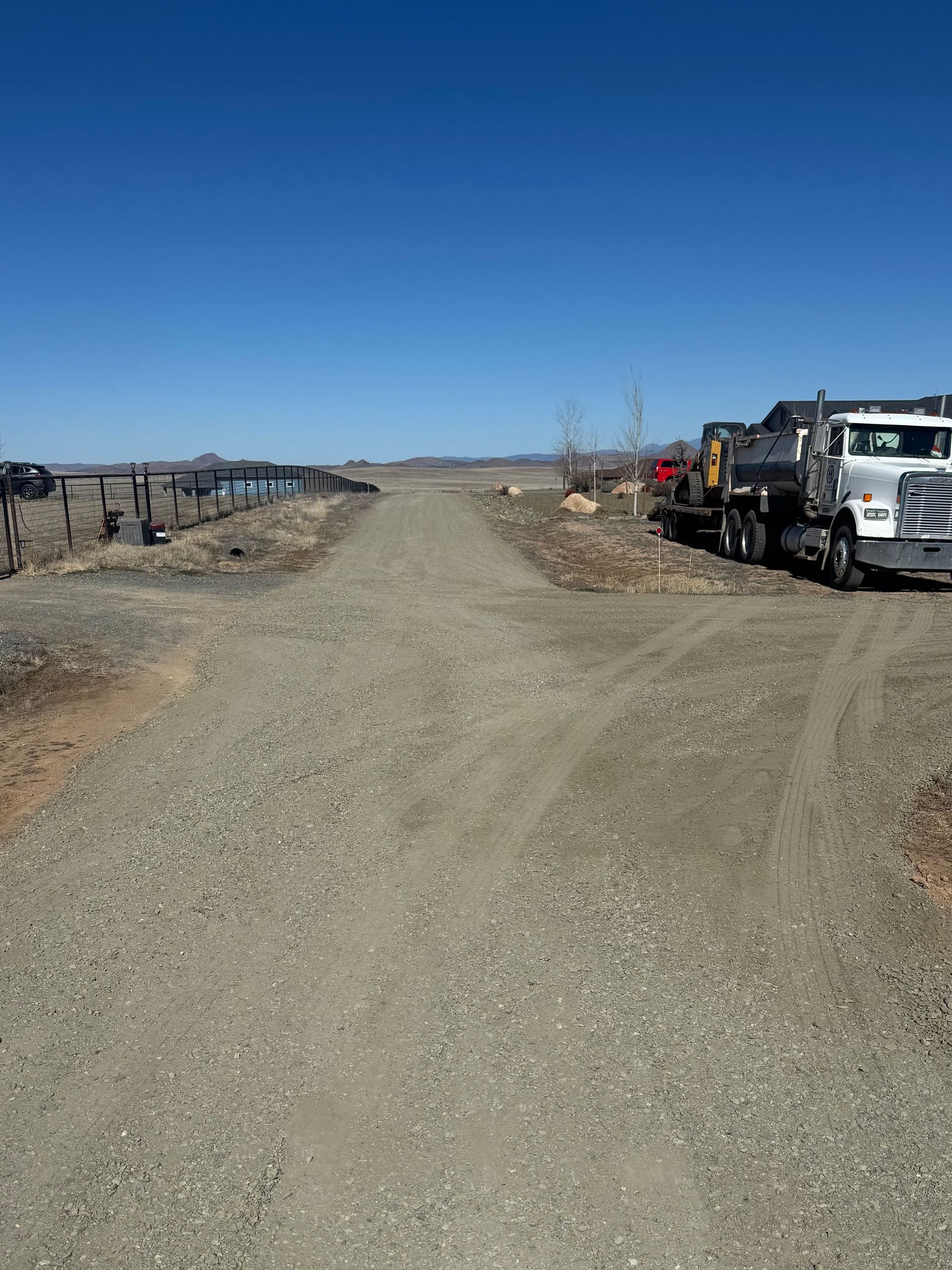 Gravel road with parked utility trucks and equipment under a clear blue sky.