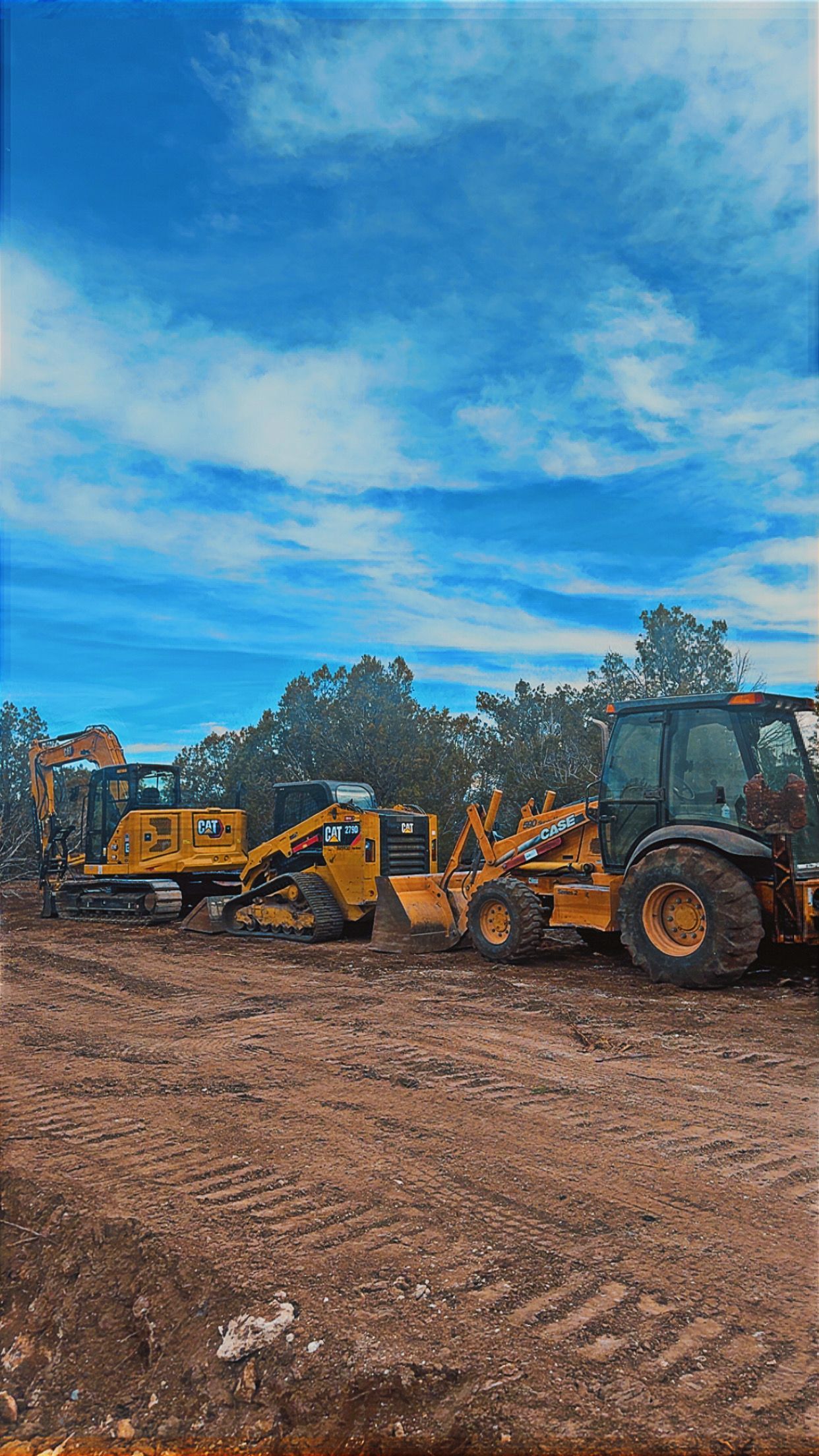 Yellow construction equipment parked on a dirt lot under a bright blue sky