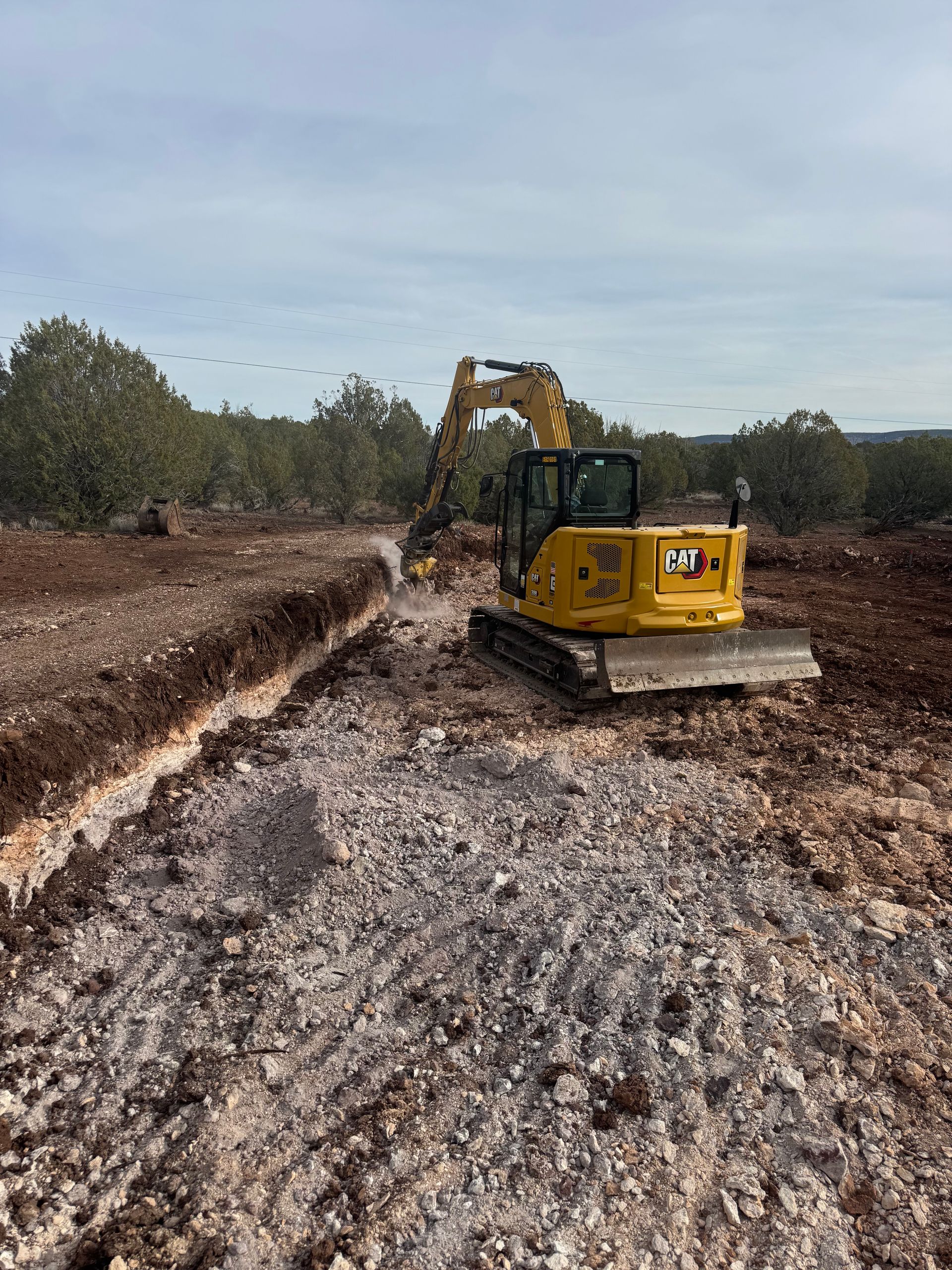 Yellow excavator grading a muddy construction site under a cloudy sky
