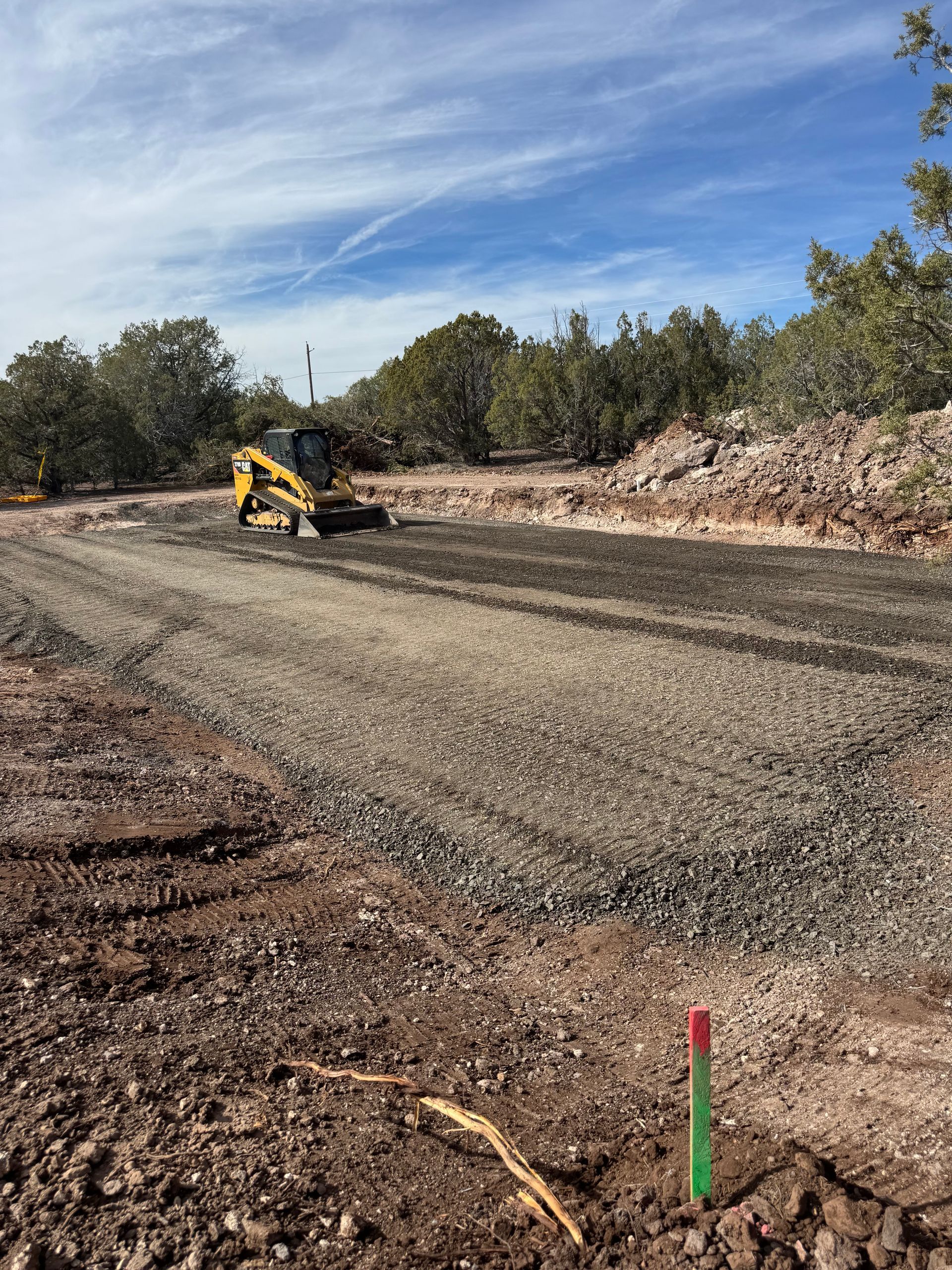 Construction site with yellow machinery grading gravel road under a blue sky