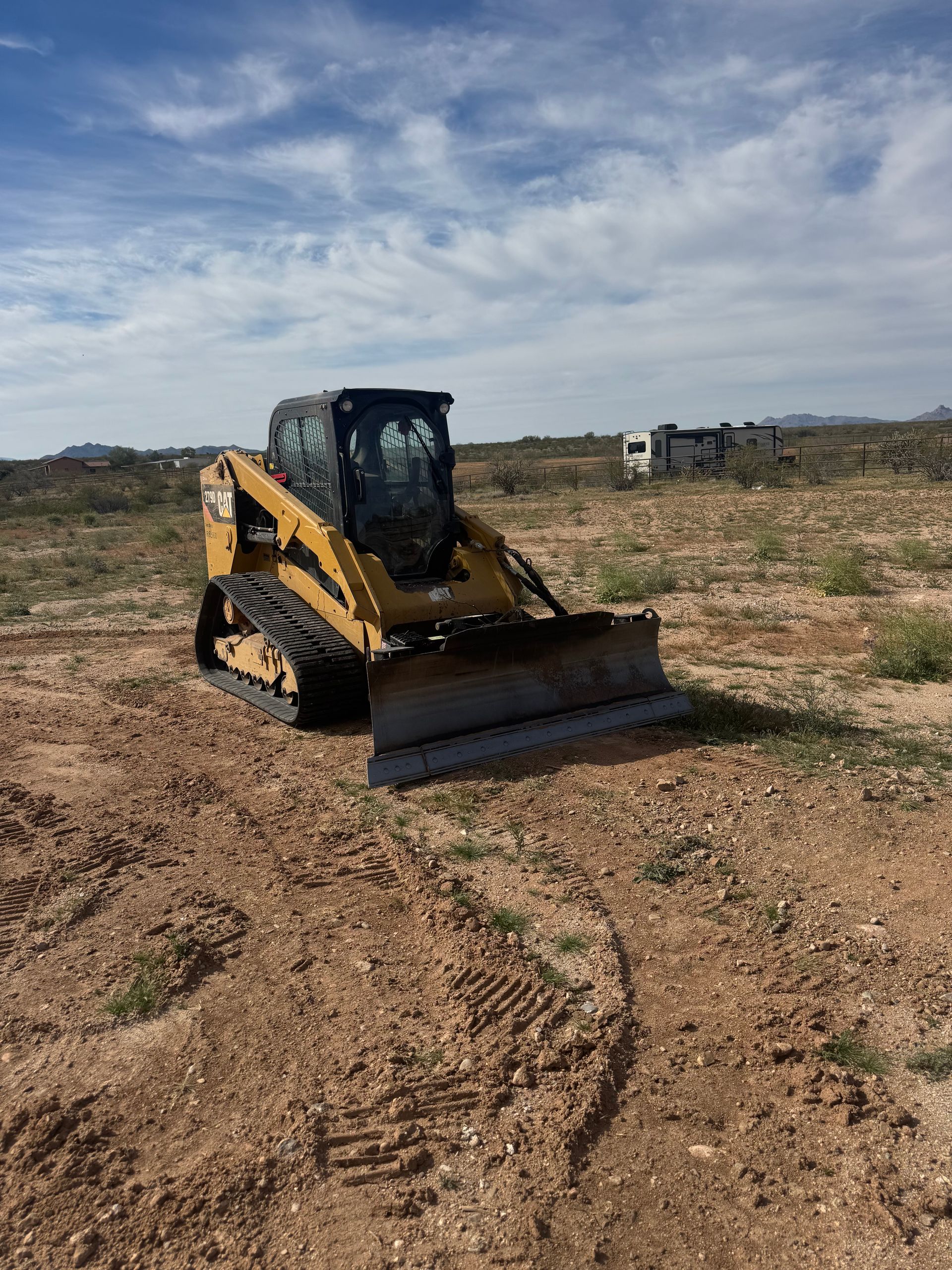 Yellow bulldozer with a front blade on a dirt field under a cloudy sky