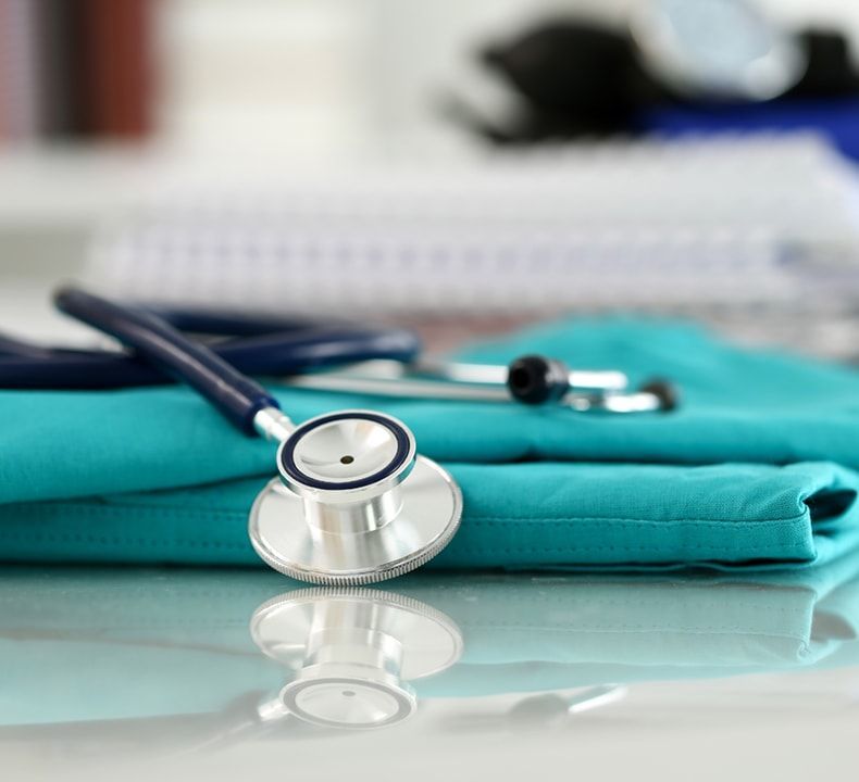 Stethoscope on teal medical scrubs, reflecting on a glass surface.