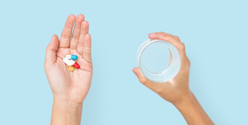 Hands holding pills and a glass of water, ready to take medication against a blue background.