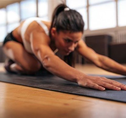 A woman is kneeling on a yoga mat in a gym.
