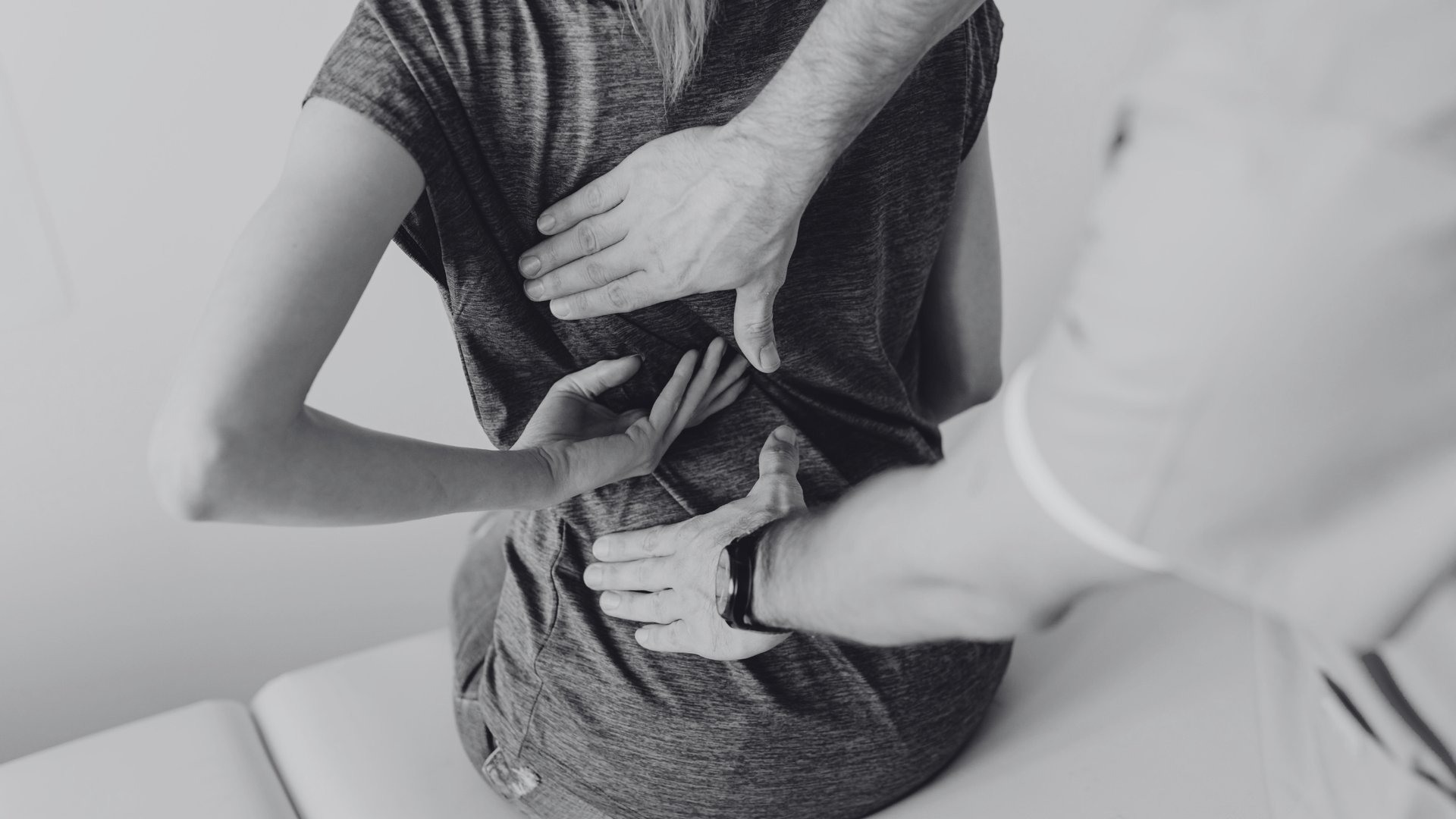 Physical therapist adjusting a seated person's back brace in black-and-white image