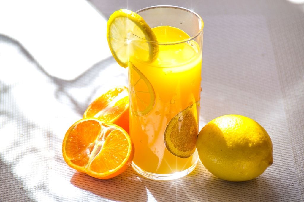 Glass of orange juice with lemon slice, tangerines, and a whole lemon on a white surface.